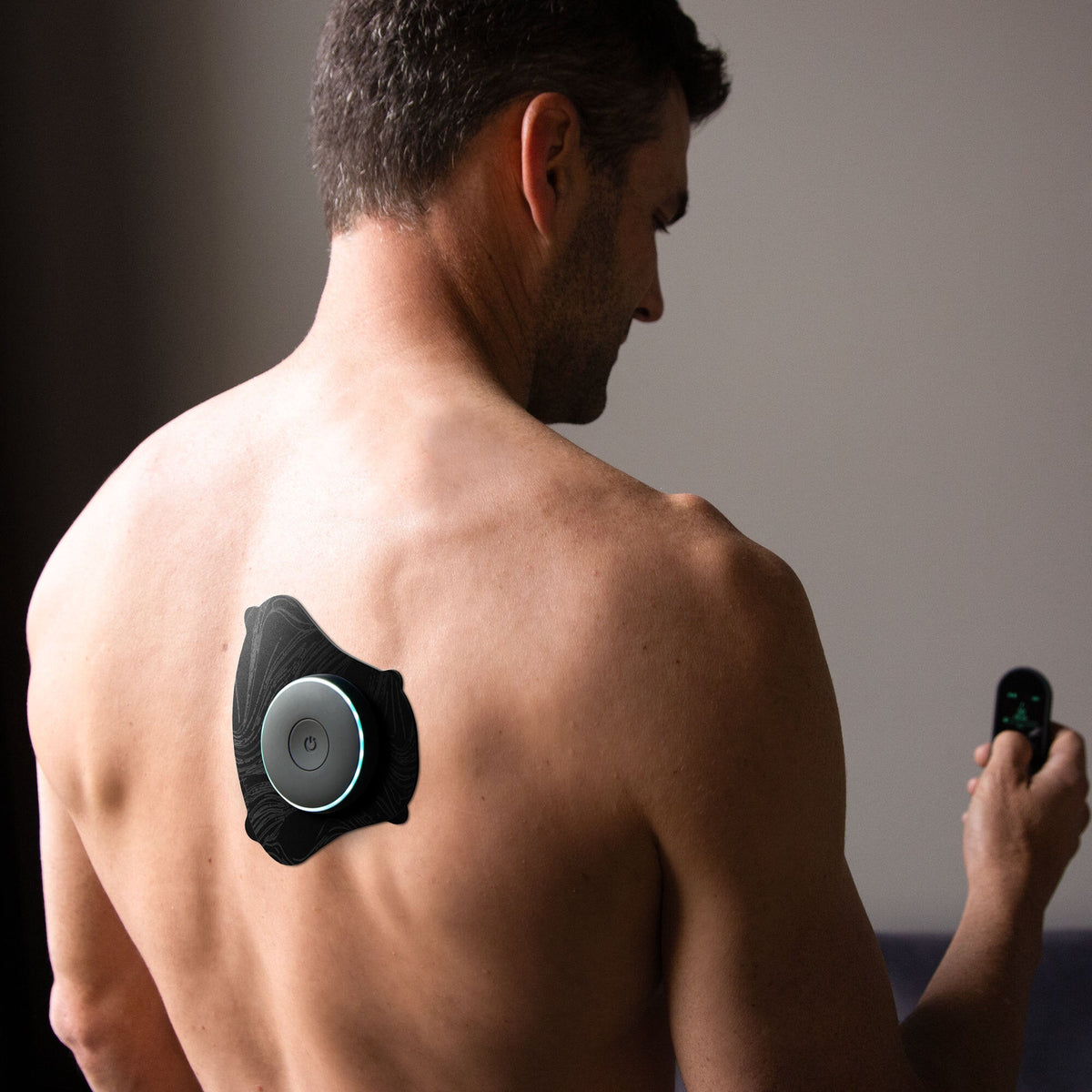 Man with a Chirp Halo™ Trap Pad Set device on his back holding a remote control against a dark background