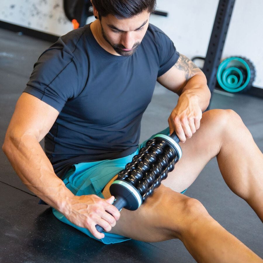 Man using a massage roller on his leg in a gym setting