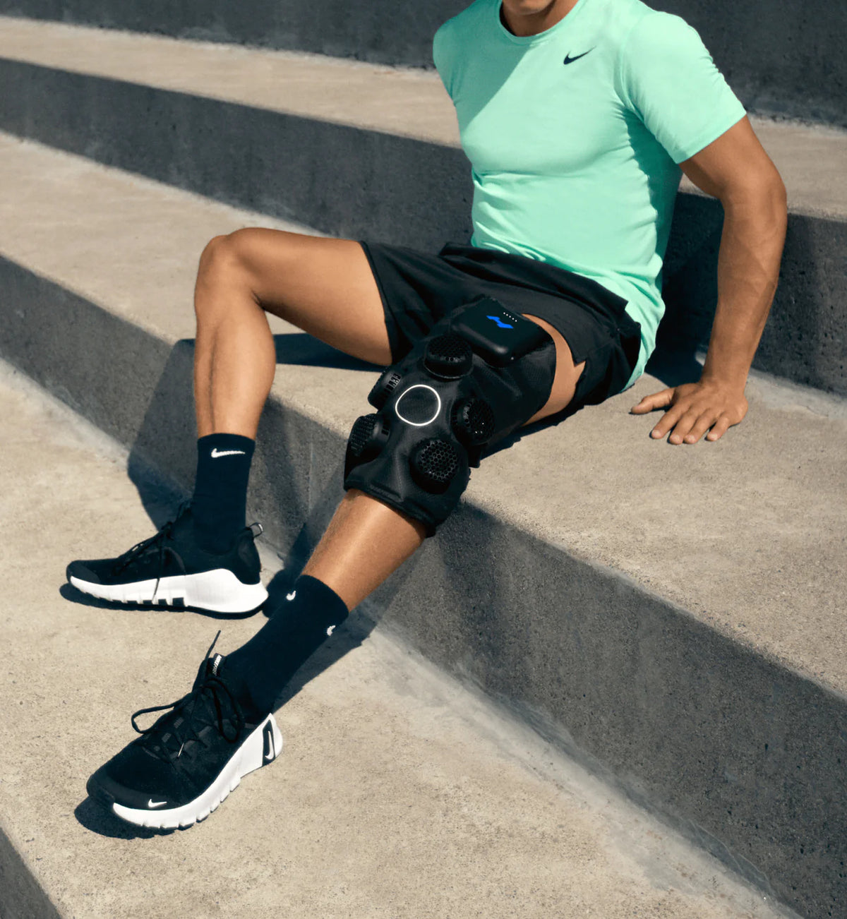 Person sitting on concrete steps wearing a Hyperice X 2 Knee device