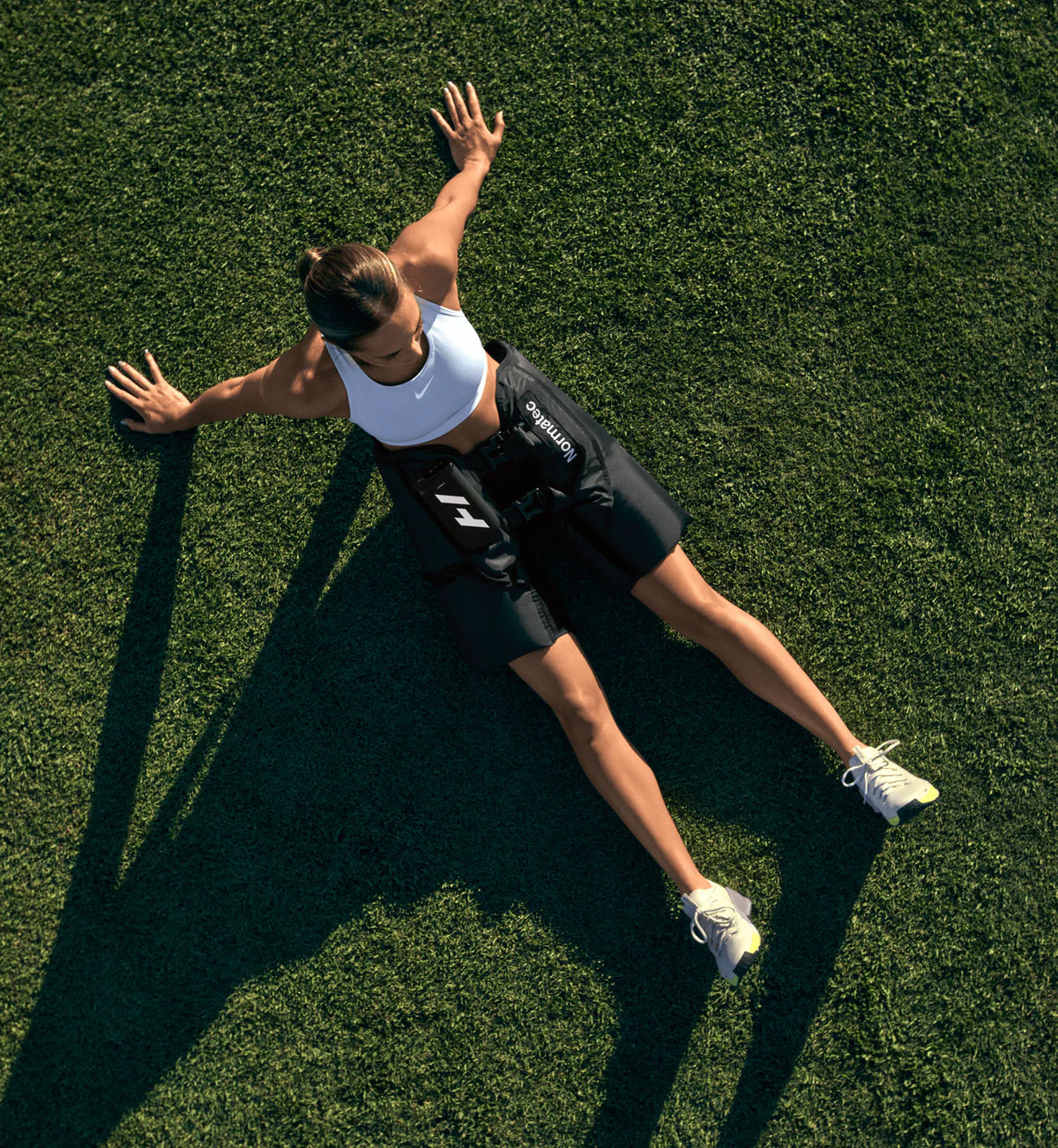 Person lying on grass and using Hyperice Normatec Elite Hips system