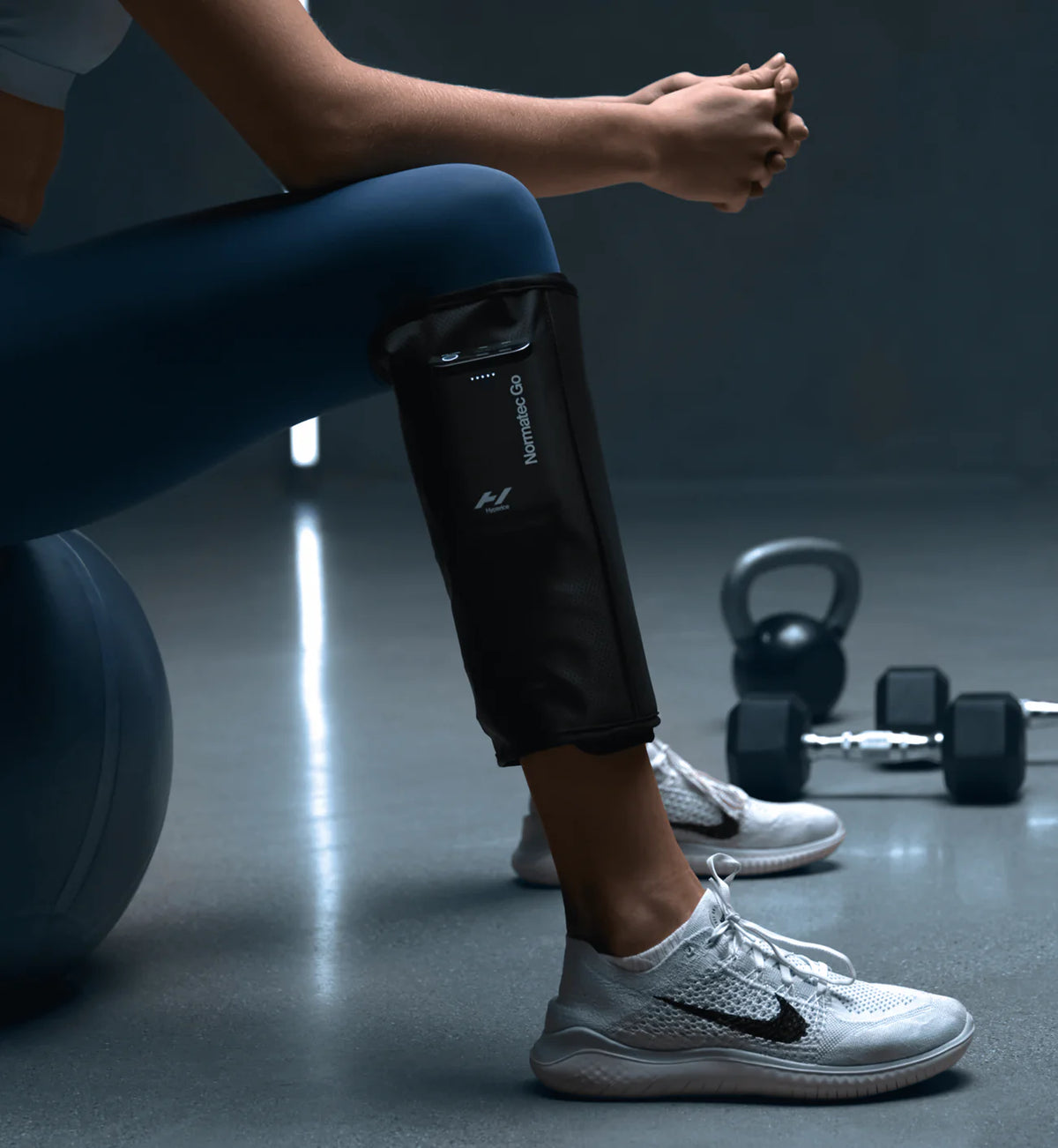 Person sitting on a gym ball using Hyperice Normatec Go portable calf compression system
