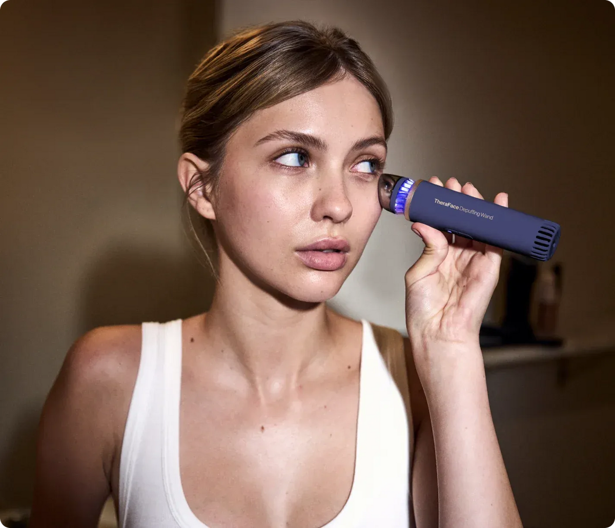 Woman using a Therabody TheraFace Depuffing Wand (Indigo) on her face
