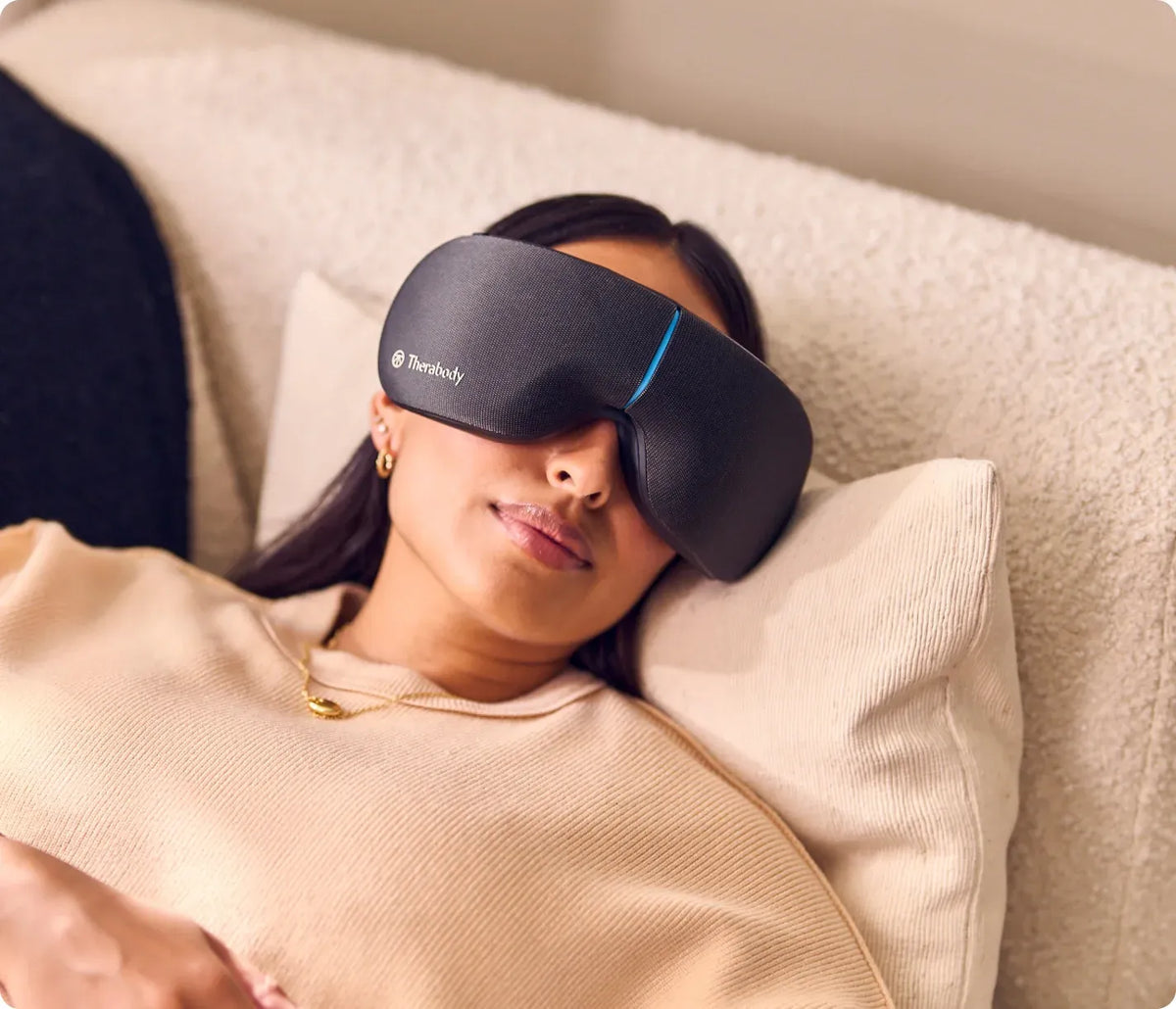 Woman wearing Therabody SmartGoggles 2nd Gen while relaxing in bed