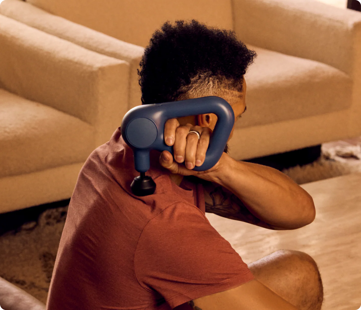 Person using a massage gun in a living room setting