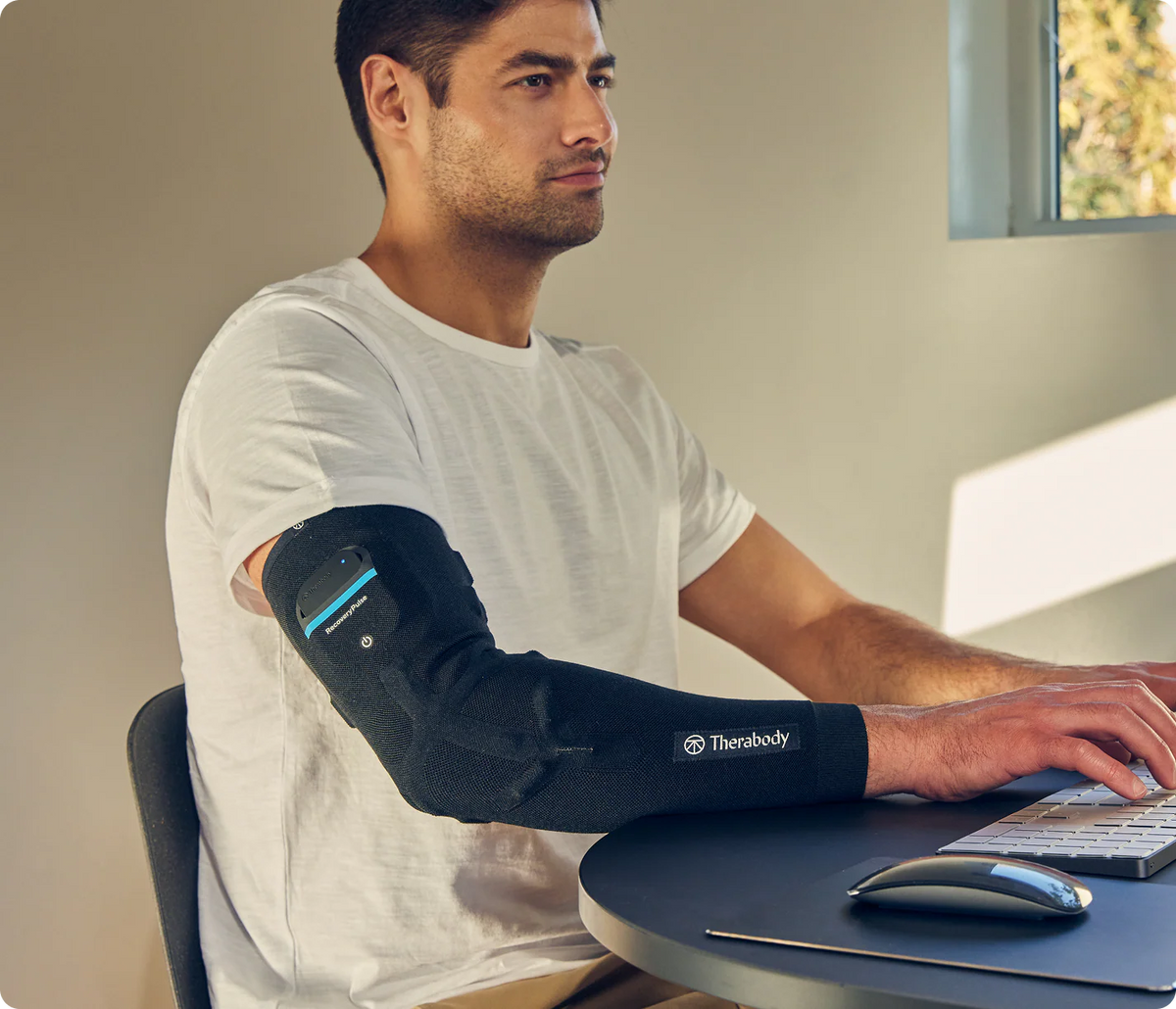 Man using Therabody RecoveryPulse Arm compression sleeve while working at a desk