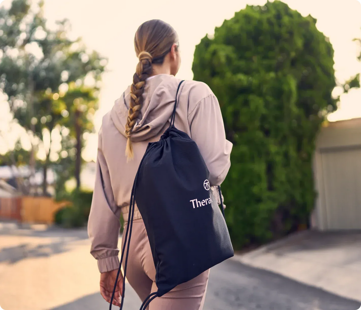 Person walking outdoors with a drawstring bag labeled Therabody