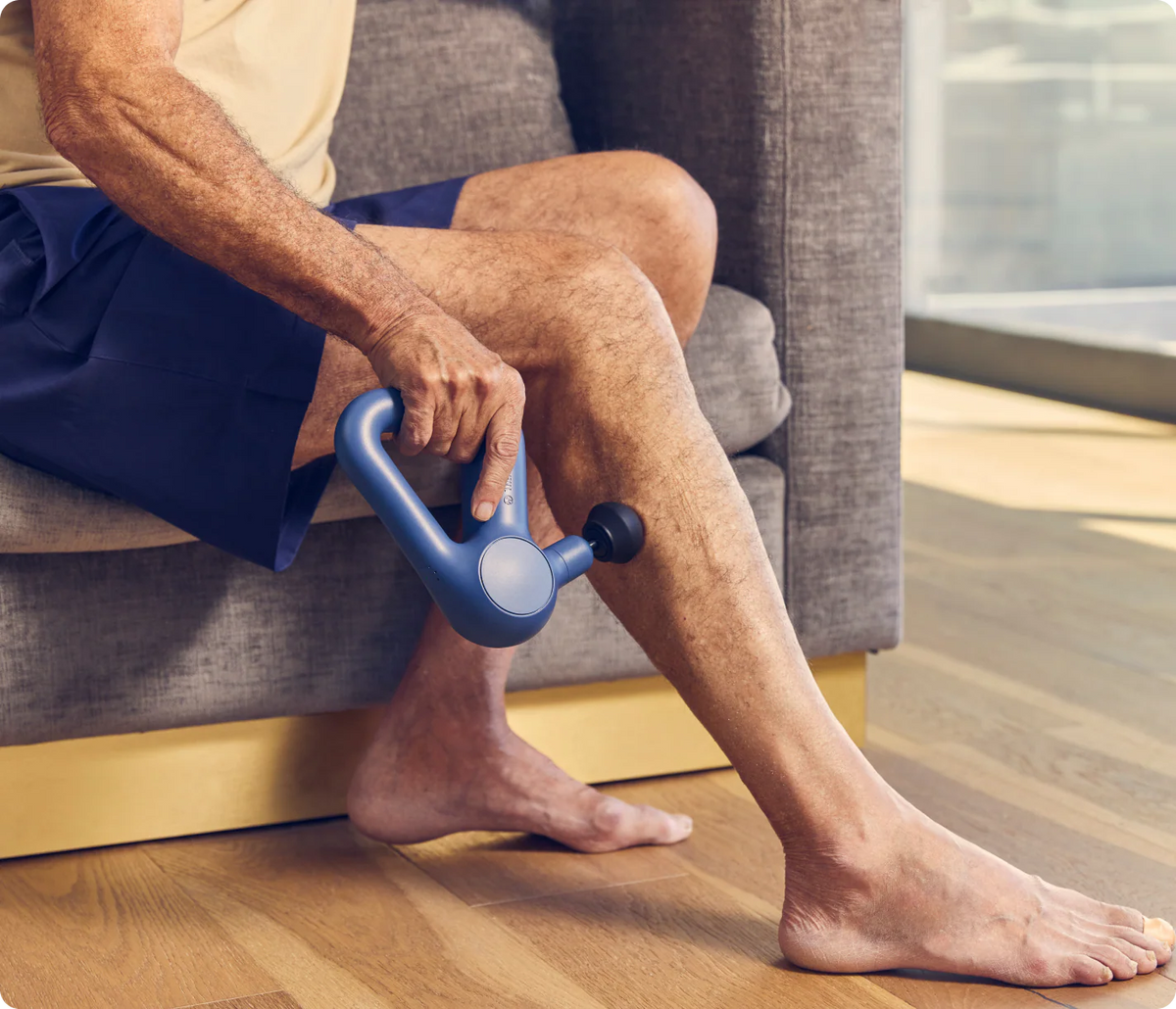 Person using Theragun Relief (Navy) Percussion Massage Gun on their leg while sitting on a couch