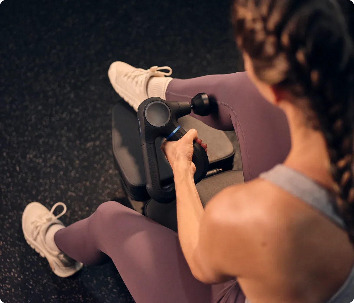 Women using a massage gun on their leg in a gym setting