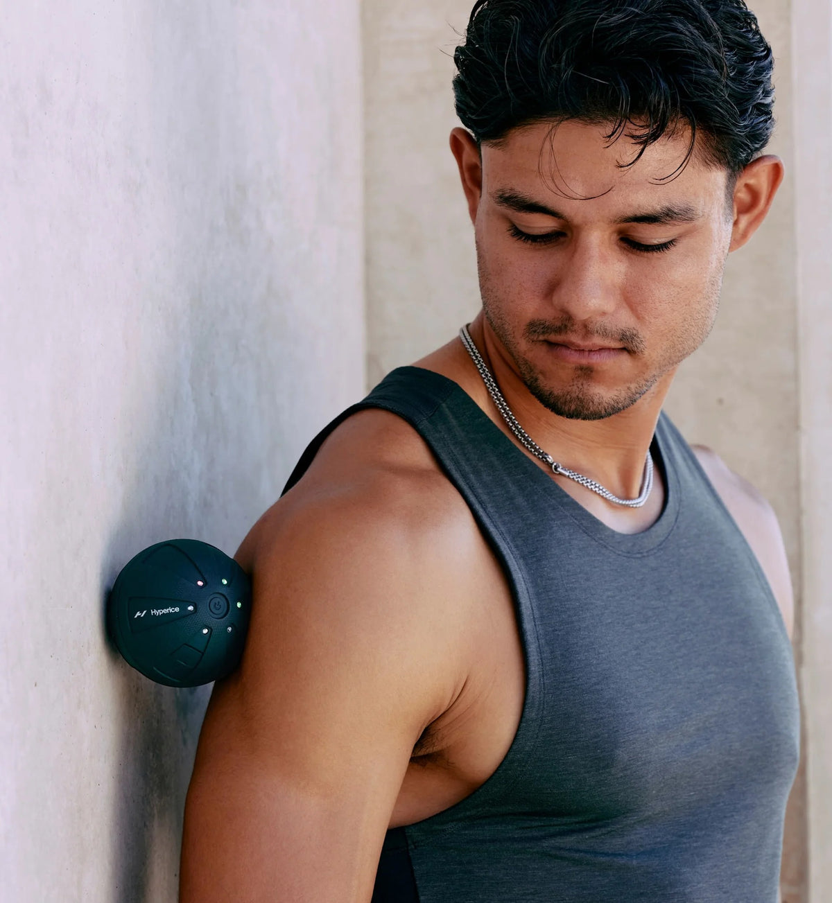 Man with a Hyperice Hypersphere Go vibrating massage ball on his arm against a wall