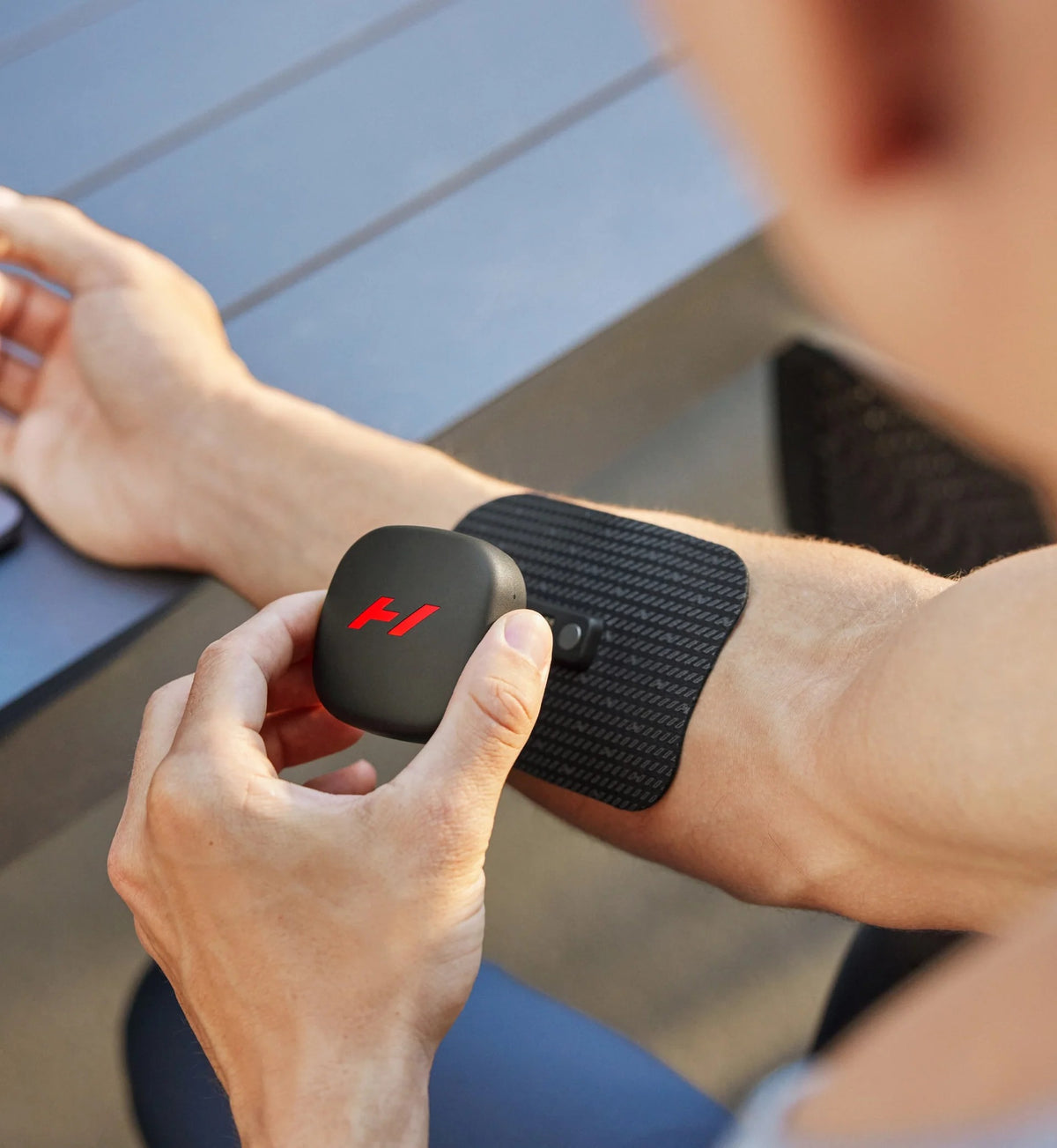 Person applying a Hyperice Venom Go wearable massager to their arm outdoors