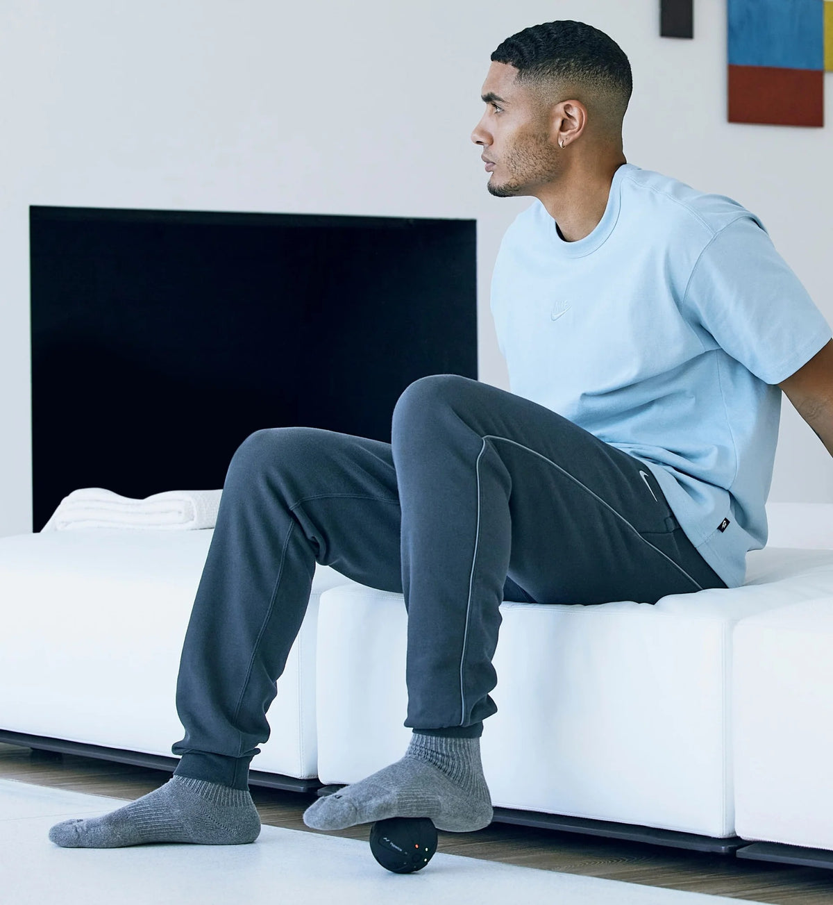 Man sitting on a white couch using a Hyperice Hypersphere Go massage ball for targeted muscle massage