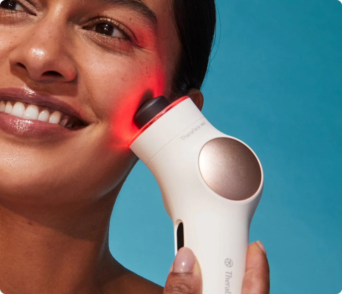 Woman using Therabody TheraFace PRO with red LED light therapy on her face