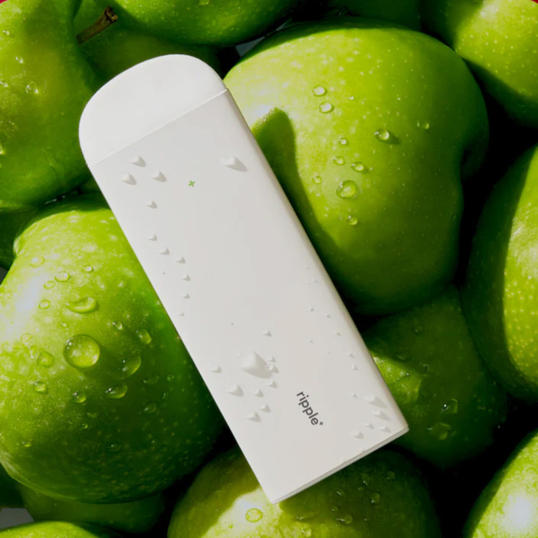 green apple flavored vape device with apples background